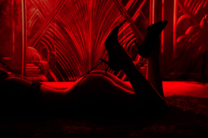 Silhouetted woman lying on stomach in red light with heels raised.